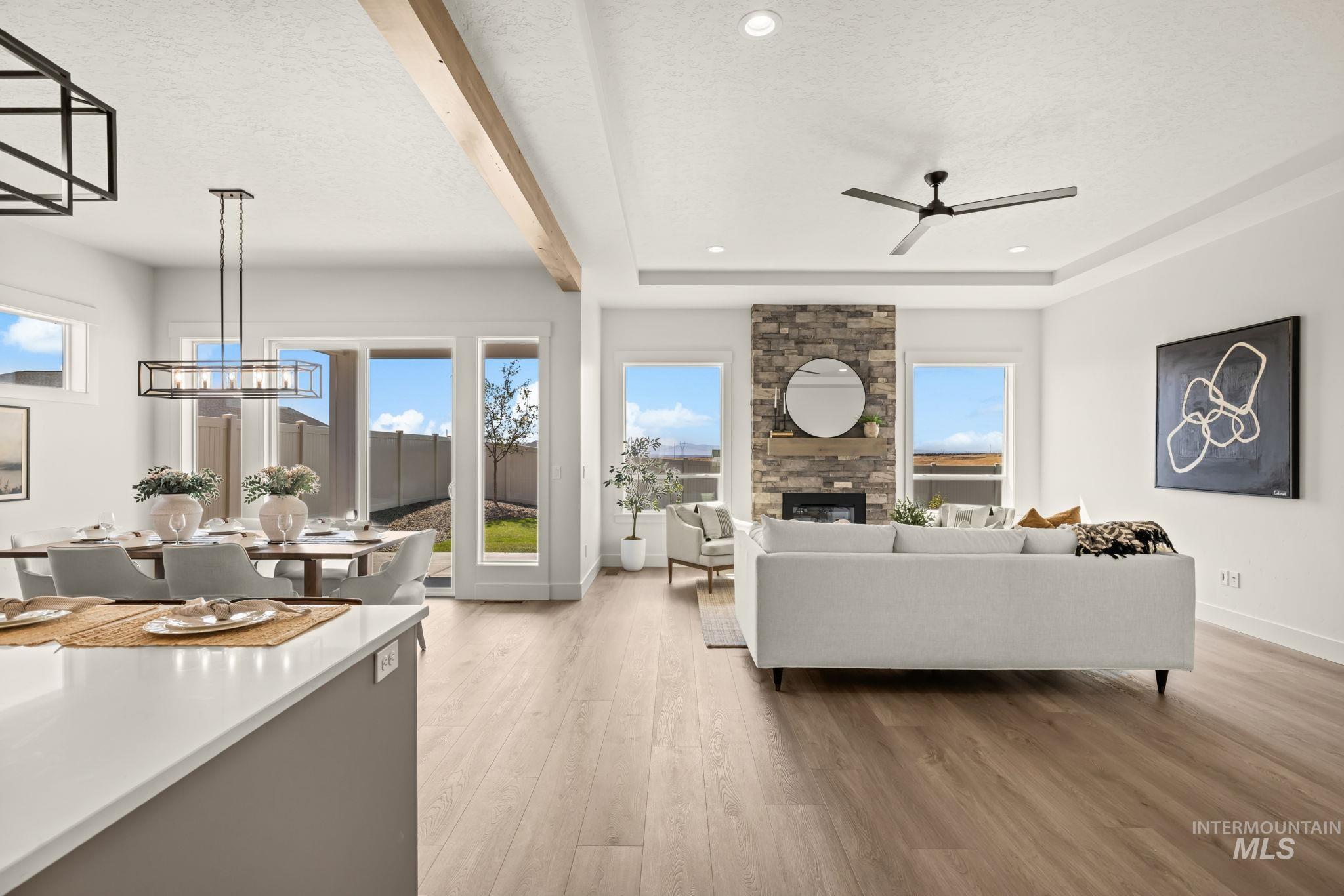 345 South Strut Way Boise, ID 83716 - Photo 11 of 50 Open-concept living space featuring wood-finish flooring, a stone-accented fireplace, and a tray ceiling