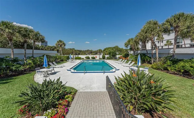 a view of a swimming pool with lawn chairs potted plants and large tree