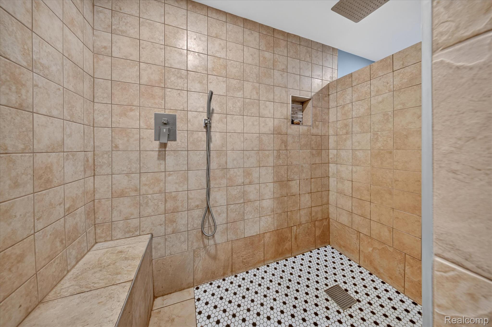 8114 Chilson Road Pinckney, MI 48169 - Photo 22 of 32 Walk-in shower featuring light-toned square wall tiles, a built-in shower bench, a recessed niche, a rain showerhead, and black and white hexagonal mosaic floor tiles