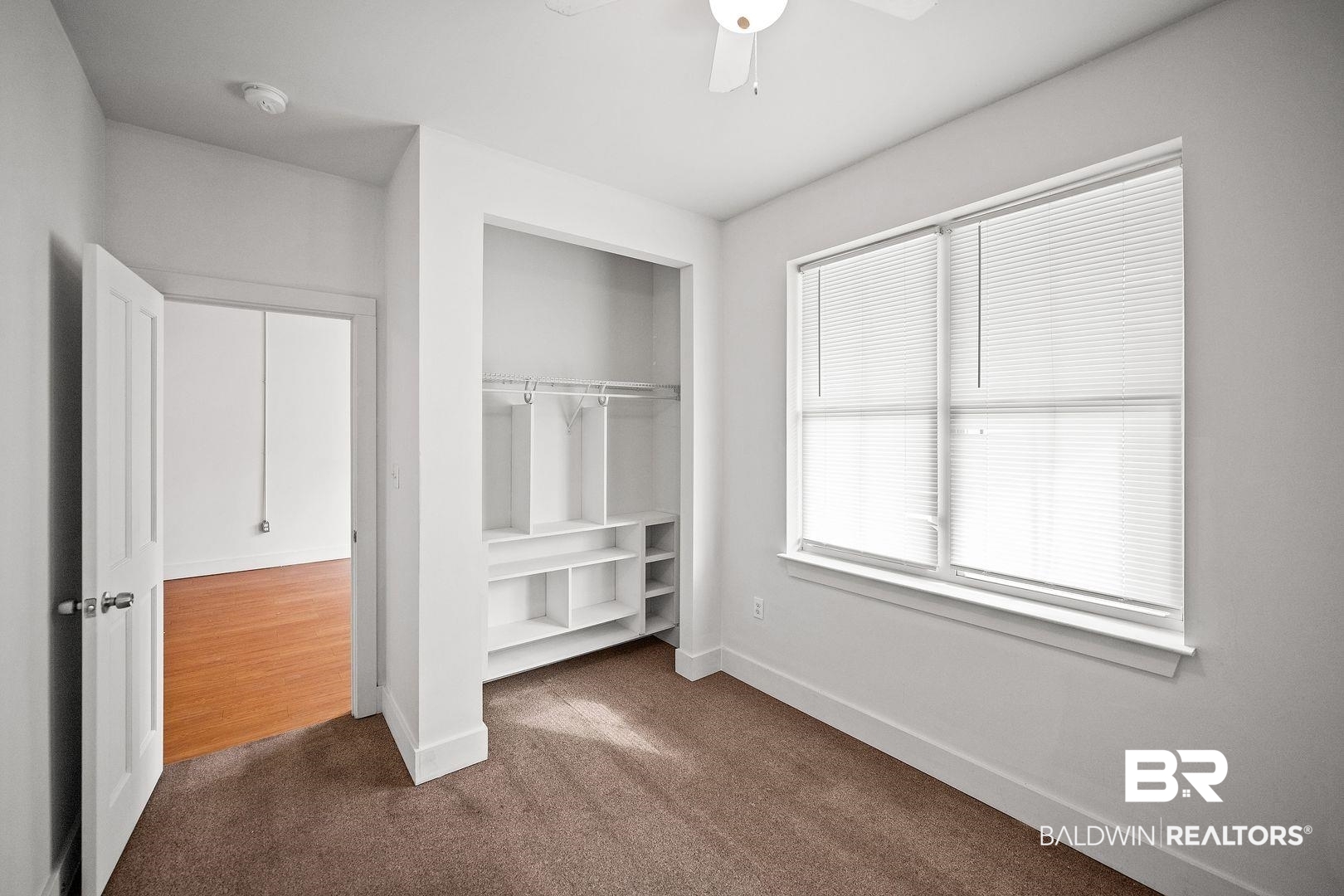 635 East Azalea Avenue Foley, AL 36535 - Photo 10 of 18 Bedroom featuring a double-pane window with blinds, a built-in closet system with shelving and hanging rods, brown carpet flooring, and a ceiling fan