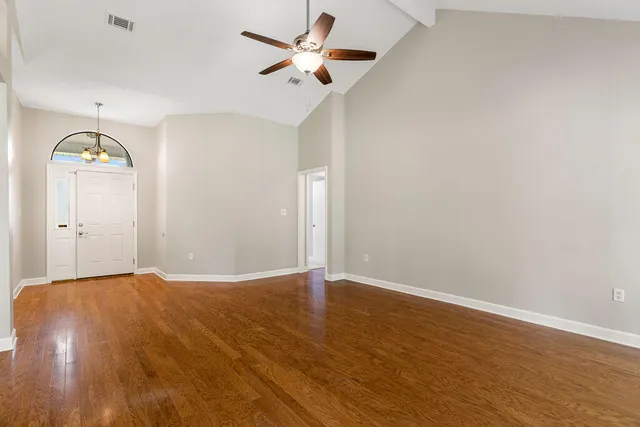 an empty room with wooden floor ceiling fan and window