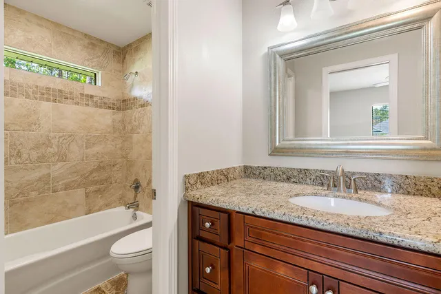 a bathroom with a granite countertop sink a toilet a mirror a bathtub and shower