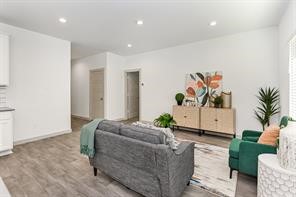 7811 Golden Rubia Lane Rosharon, TX 77583 - Photo 5 of 10 The photo showcases a modern, open living room with neutral walls and wood-style flooring. It features a cozy gray sofa, green armchair, and a stylish sideboard with plants and artwork, creating a welcoming atmosphere.