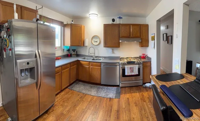 a kitchen with stainless steel appliances granite countertop a refrigerator a sink dishwasher a stove and white countertops with wooden floor