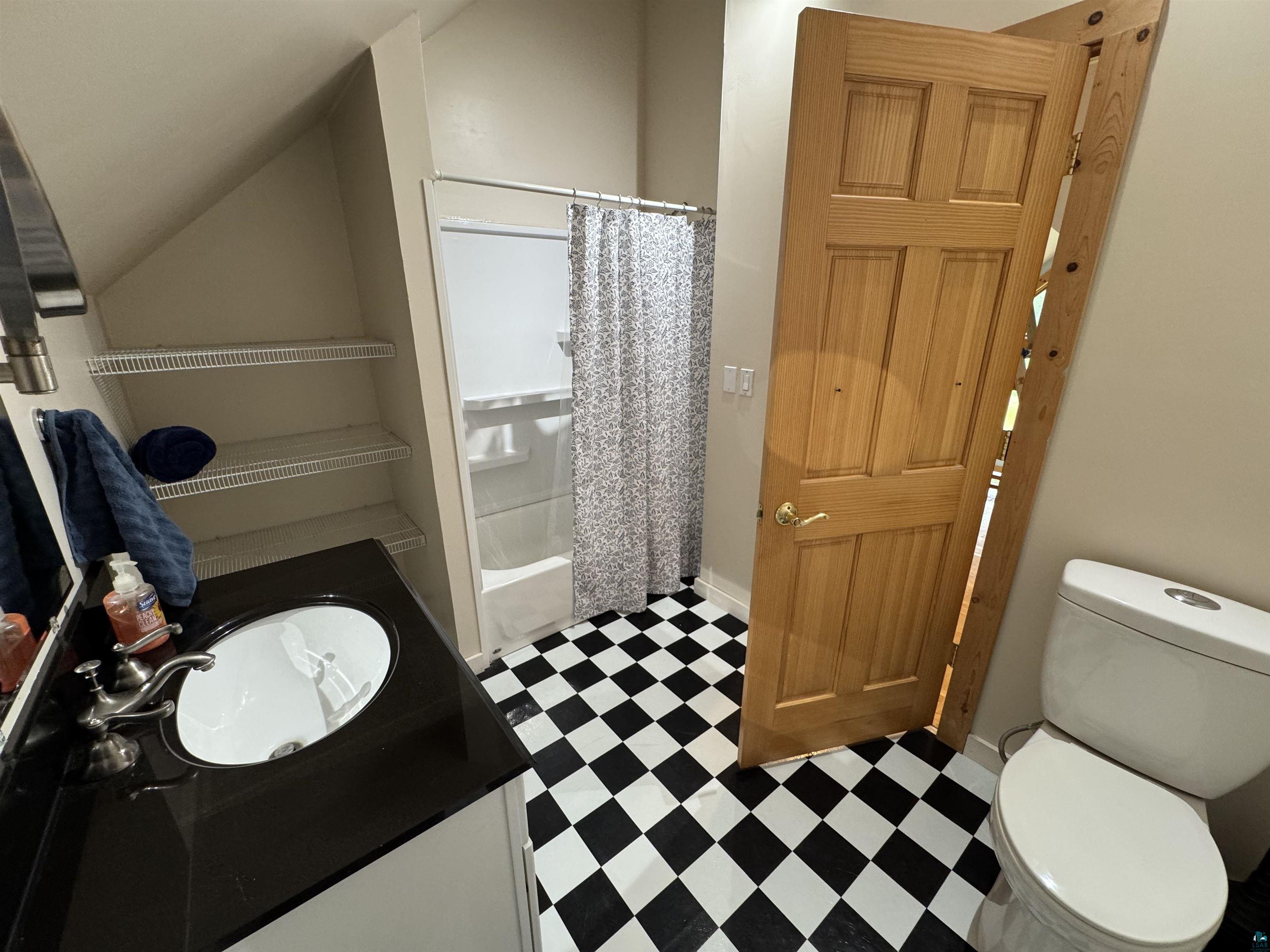 1745 Becks Road Maple, WI 54854 - Photo 24 of 46 Upper level Bathroom featuring a black and white checkered floor, a white vanity with a black countertop, a white oval sink with a dual-handle faucet, a built-in shower/tub combination, and open shelving