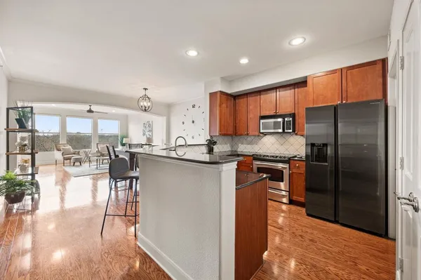 a kitchen with stainless steel appliances granite countertop a refrigerator a stove a sink a dining table and chairs with wooden floor