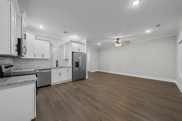 a large kitchen with stainless steel appliances granite countertop a sink a stove a refrigerator and white cabinets with wooden floor