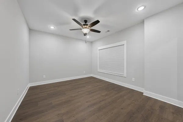an empty room with wooden floor ceiling fan and windows