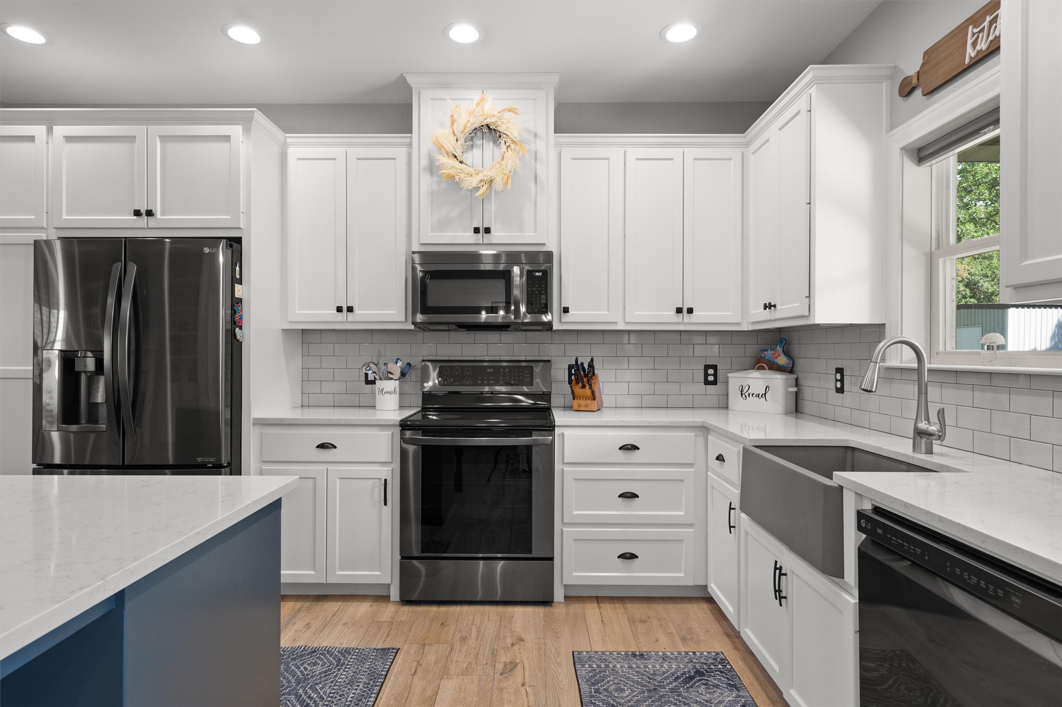 136 Fawn Hollow Elgin, TX 78621 - Photo 10 of 40 Modern kitchen featuring white shaker cabinetry, stainless steel appliances, light wood-finish flooring, a farmhouse-style sink, and light countertops