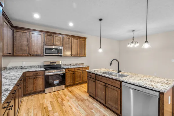 a kitchen with stainless steel appliances granite countertop a sink a stove top oven a refrigerator with wooden floors and cabinets