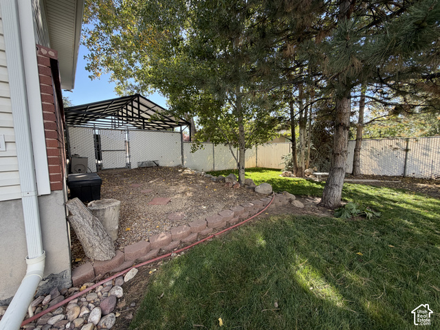 1750 West 4100 North Helper, UT 84526 - Photo 44 of 50 Spacious backyard oasis featuring mature shade trees, a brick-bordered planting bed, manicured lawn, metal pergola structure, and secure fencing