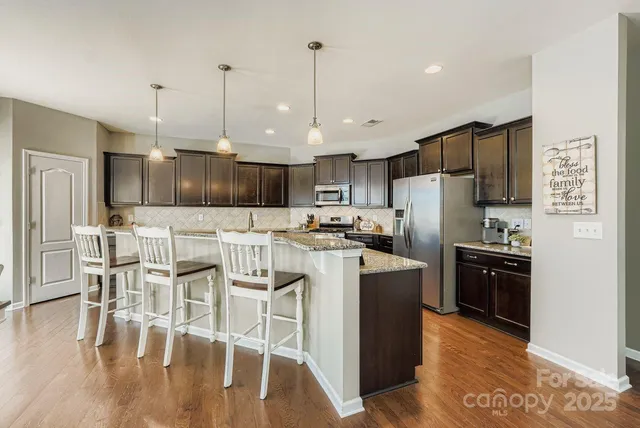 a kitchen with stainless steel appliances kitchen island granite countertop a refrigerator a stove top oven a sink dishwasher and white cabinets with wooden floor
