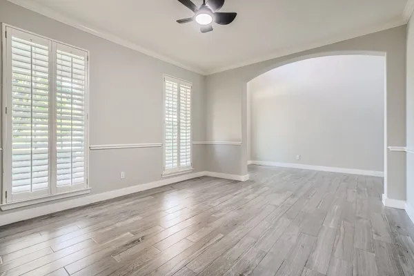 an empty room with wooden floor chandelier fan and windows