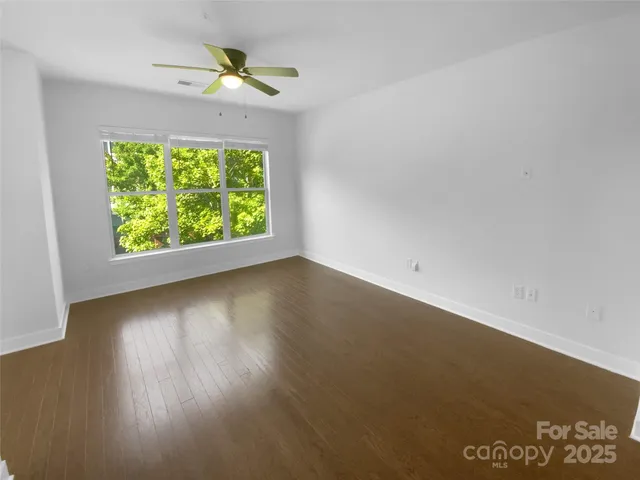 an empty room with wooden floor chandelier fan and windows