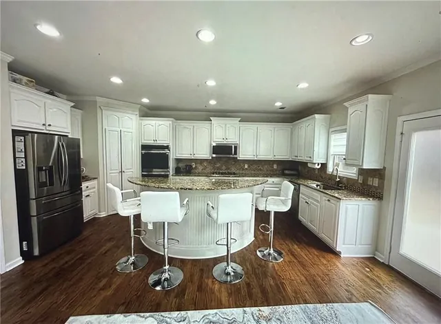a kitchen with stainless steel appliances kitchen island granite countertop a sink refrigerator and cabinets