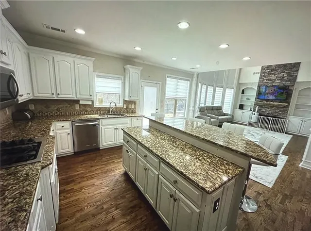 a large kitchen with stainless steel appliances granite countertop a stove top oven a sink dishwasher and cabinets with wooden floor