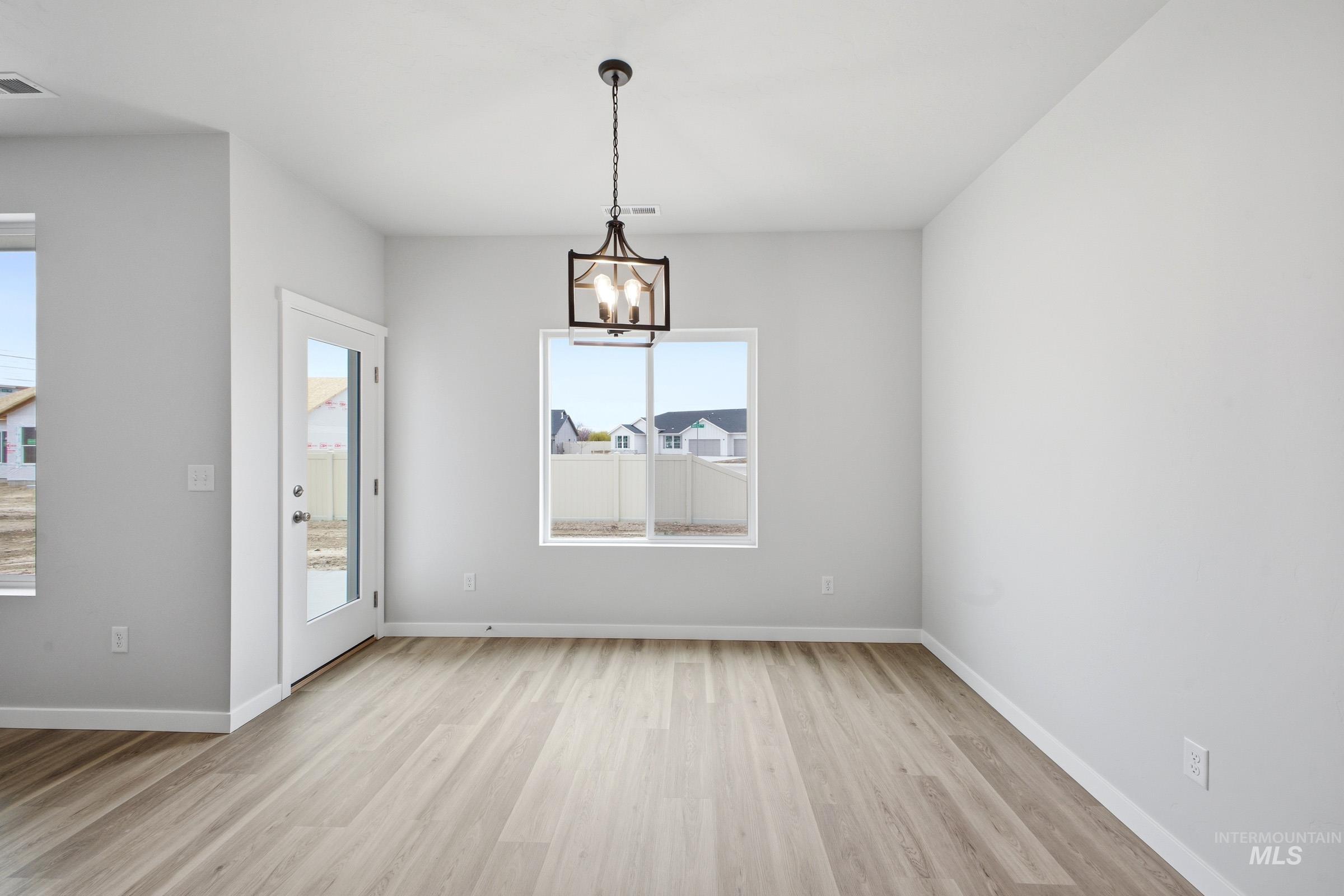 14104 Shiny Spruce Street Caldwell, ID 83607 - Photo 6 of 20 Open-concept room featuring light wood-finish flooring, a contemporary chandelier, multiple windows, and a glass-paneled exterior door