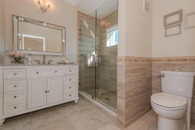 a bathroom with a toilet a sink a glass door a shower a mirror a vanity and window