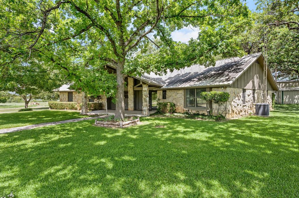 515 New Highland Road Springtown, TX 76082 - Photo 1 of 38 Stone facade residence with a pitched roofline, large picture windows, mature shade trees, and a concrete walkway