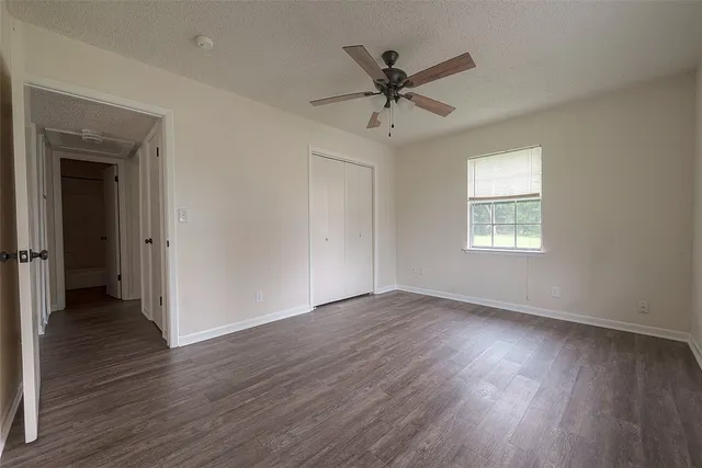 a view of an empty room with wooden floor and a ceiling fan