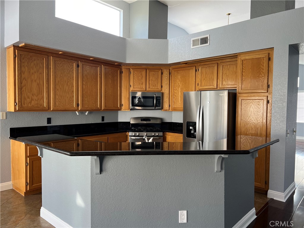 7461 Red Clover Way Highland, CA 92346 - Photo 16 of 35 a kitchen with stainless steel appliances granite countertop a refrigerator a stove and a sink with wooden cabinets