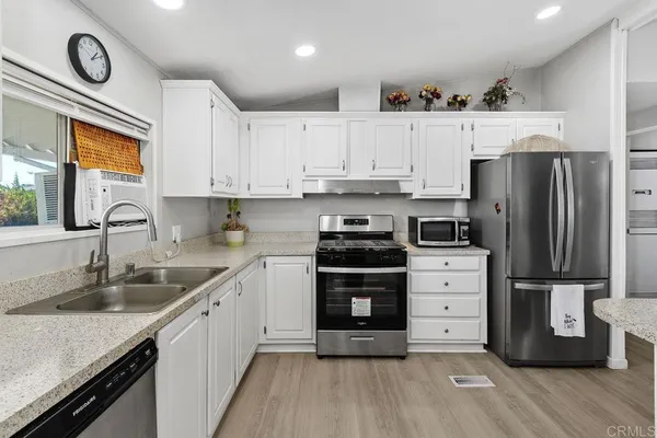 a open kitchen with stainless steel appliances granite countertop a refrigerator a sink dishwasher and white cabinets with wooden floor