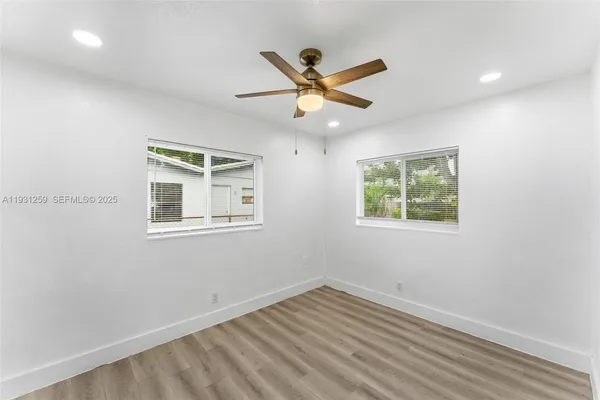 an empty room with wooden floor ceiling fan and windows