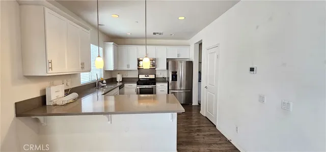 a kitchen with stainless steel appliances granite countertop a refrigerator a sink dishwasher a oven with white cabinets and wooden floor