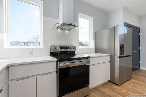 a kitchen with a stove a sink a refrigerator and white cabinets with wooden floor