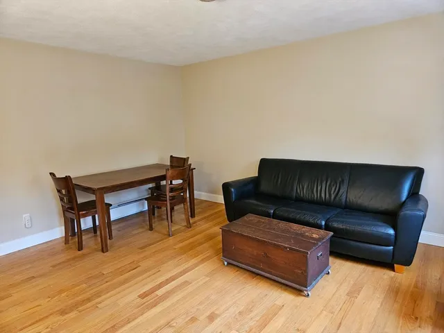 a living room with couch and a dining table with wooden floor