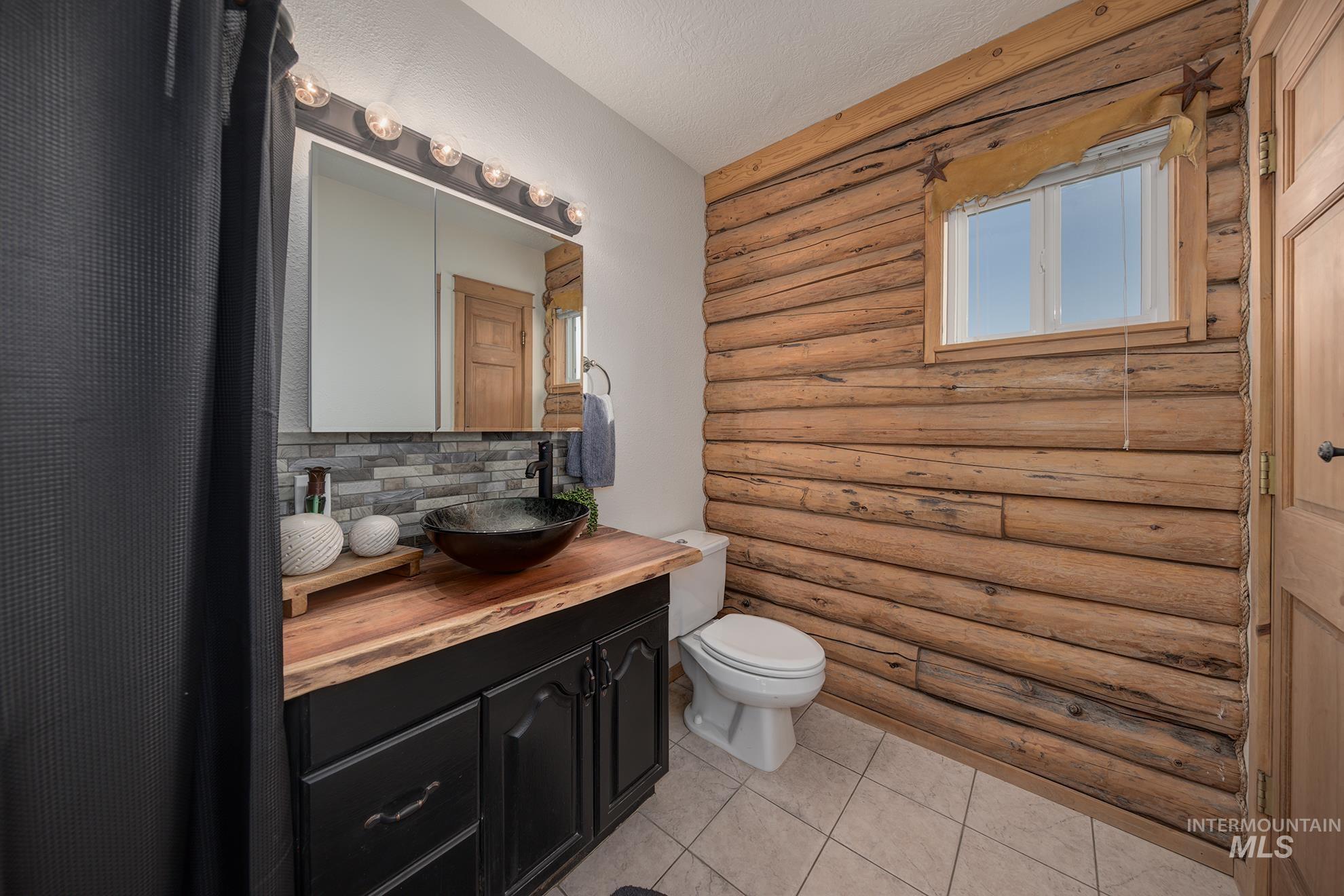 1855 Jones Road Weiser, ID 83672 - Photo 15 of 33 Bathroom with rustic walls, vanity, light tile patterned flooring, a textured ceiling, and tasteful backsplash