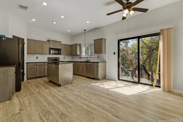 a kitchen with stainless steel appliances granite countertop a stove top oven a sink dishwasher a refrigerator and white cabinets with wooden floor next to windows