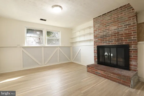 an empty room with wooden floor fireplace and windows
