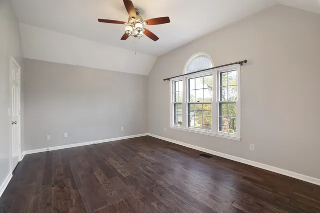 an empty room with wooden floor fan and windows