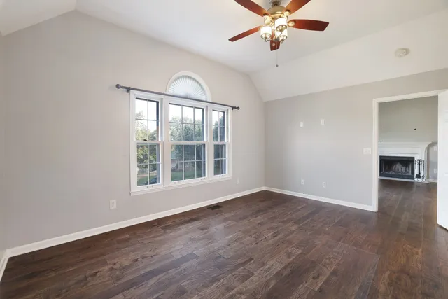 an empty room with wooden floor chandelier fan and windows