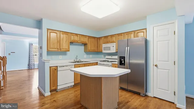 a kitchen with stainless steel appliances granite countertop a refrigerator a sink a stove and white cabinets with wooden floor