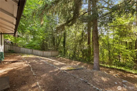 a backyard of a house with large trees and wooden fence