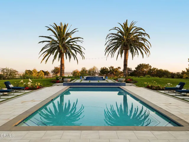 a view of swimming pool with seating space and trees in the background