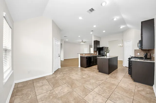 a view of kitchen with stainless steel appliances kitchen island granite countertop a stove top oven a sink dishwasher and white cabinets with wooden floor
