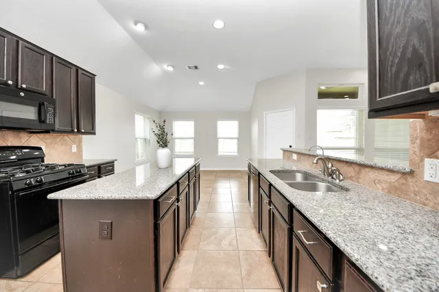 a kitchen with granite countertop kitchen island stainless steel appliances a sink stove top oven and cabinets