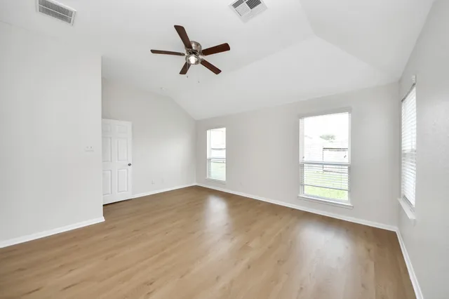 an empty room with wooden floor fan and windows