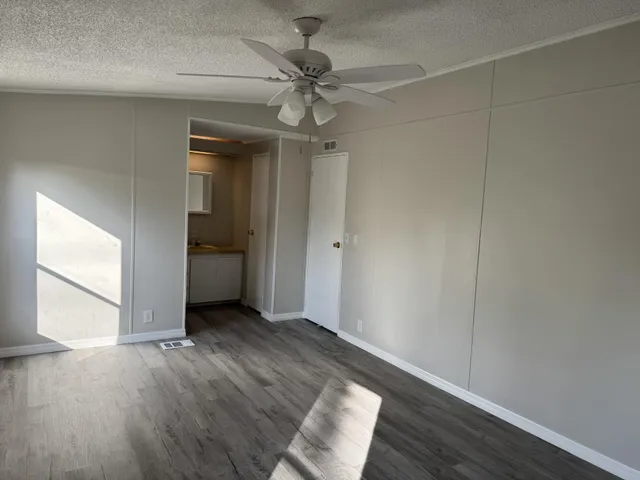 an empty room with wooden floor chandelier fan and windows