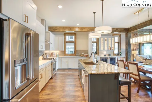 a kitchen with stainless steel appliances granite countertop a refrigerator a sink dishwasher a dining table and chairs with wooden floor