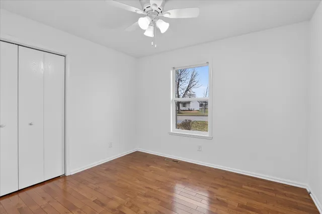 an empty room with wooden floor closet and windows