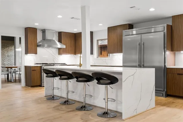 a kitchen with stainless steel appliances granite countertop a sink a stove a refrigerator and chairs