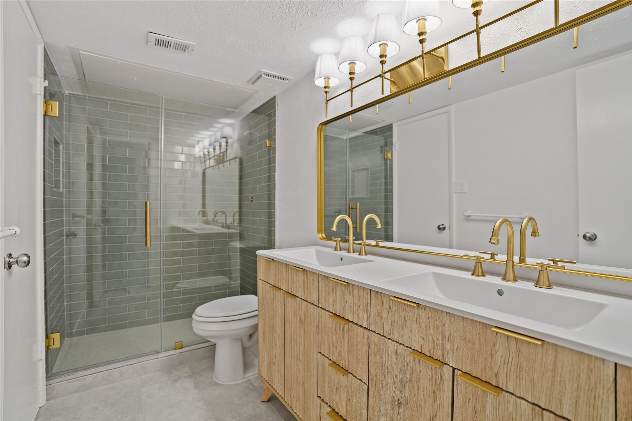 6610 Blue Ridge Drive Richmond, TX 77469 - Photo 15 of 24 Modern bathroom featuring a double vanity with gold fixtures, elegant lighting, large mirror and a spacious glass-enclosed shower with stylish tilework.