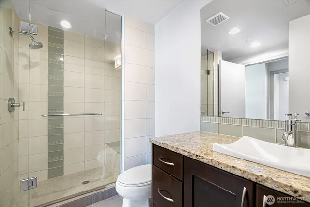 a bathroom with a granite countertop sink a toilet a mirror and shower