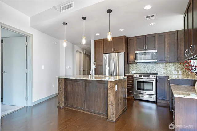 a kitchen with stainless steel appliances granite countertop a stove a sink a refrigerator and a wooden floor