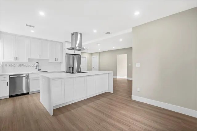 a kitchen with stainless steel appliances granite countertop a stove top oven a sink and white cabinets with wooden floor