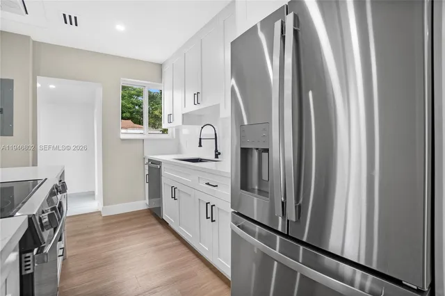 a kitchen with stainless steel appliances granite countertop a refrigerator a sink and white cabinets